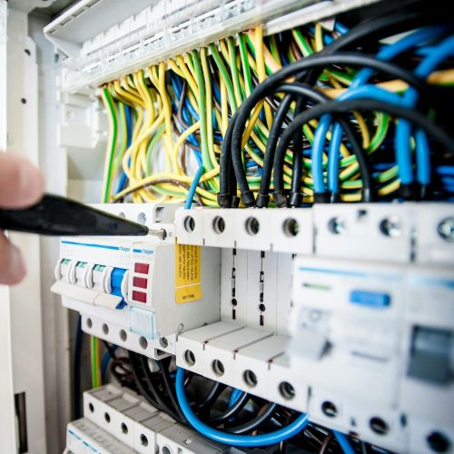 Hand of electrician working on a circuit breaker panel with colorful wires, ensuring safe electrical connections.